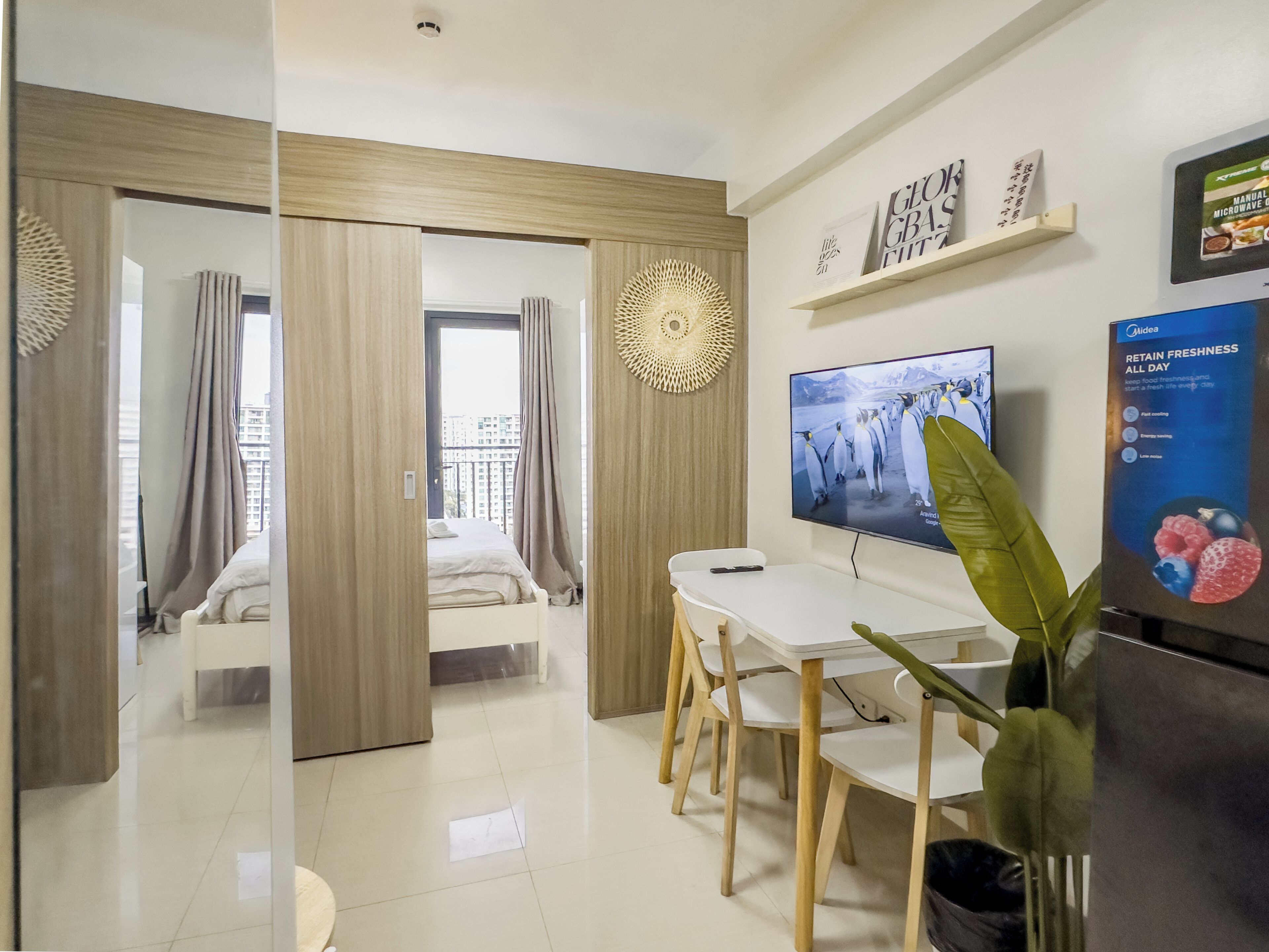 Una habitación de hotel moderna con una cama, un comedor con mesa y sillas, un televisor y una planta.