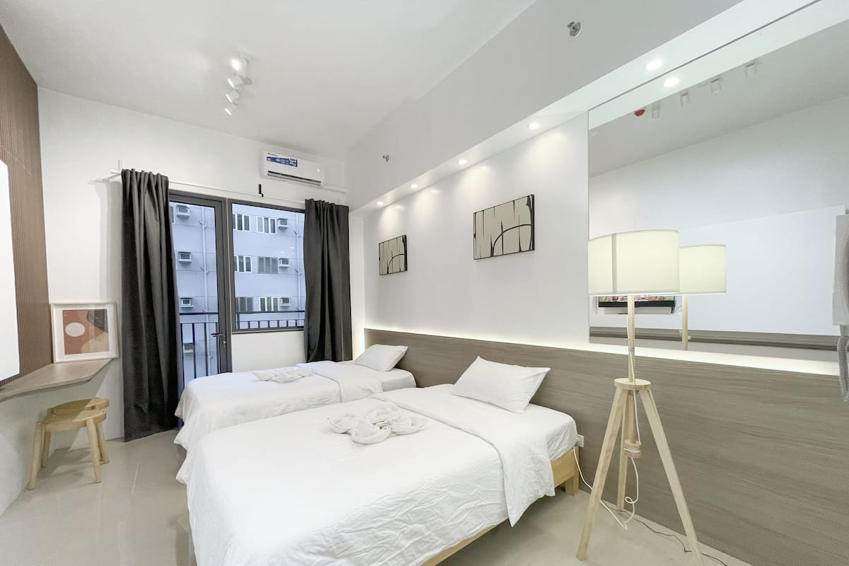 Una habitación de hotel moderna con dos camas, un escritorio, una lámpara de pie y un espejo grande.