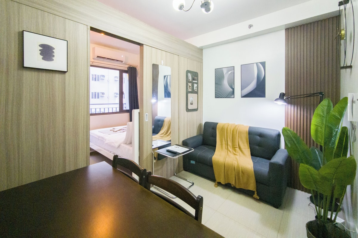 Una habitación de hotel con cama, sofá, mesa de comedor y una planta grande.