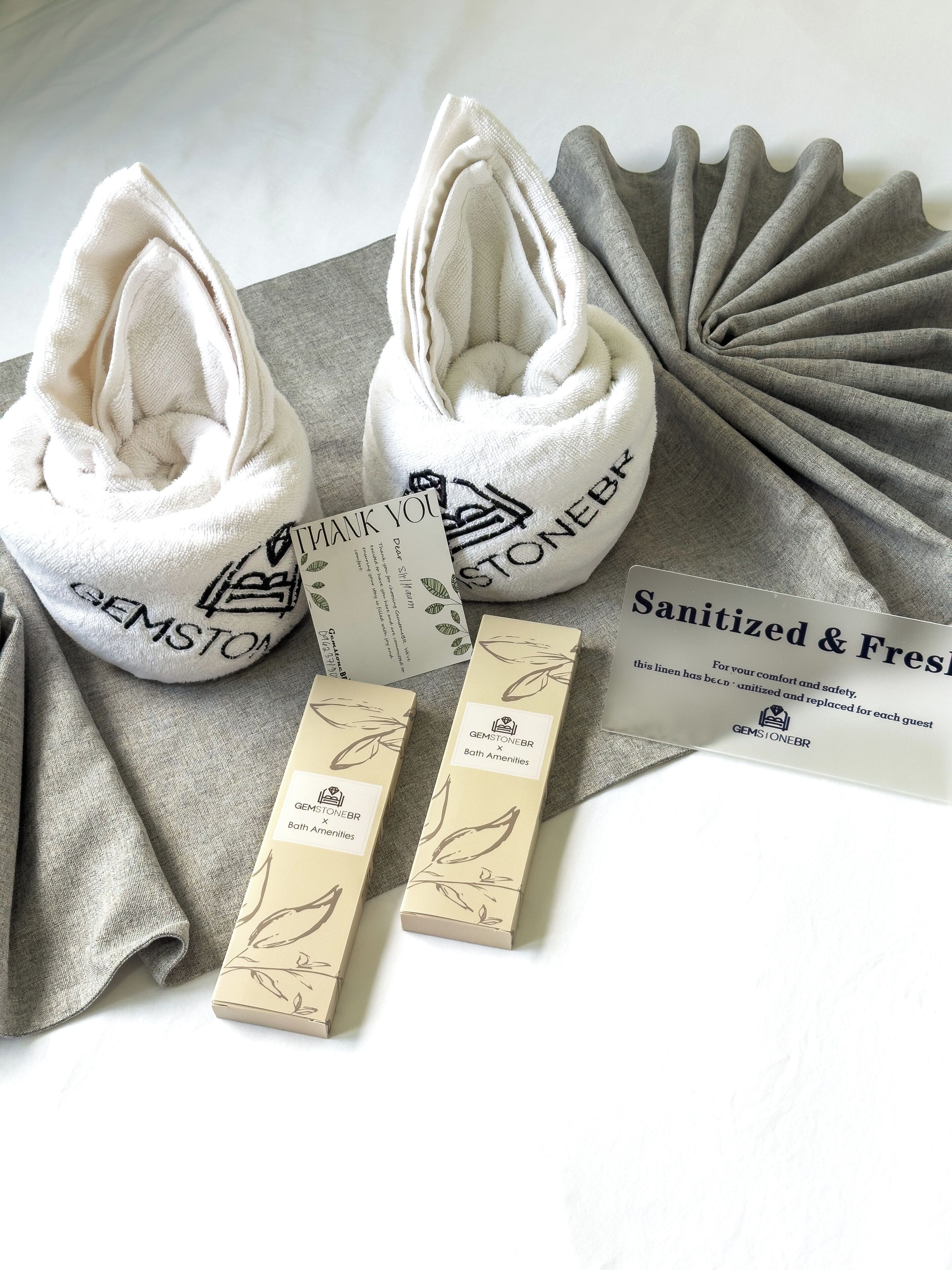 A towel, a thank you card, and a box with a leaf pattern, all labeled 'GEMSTONEBR Bath Amenities.'