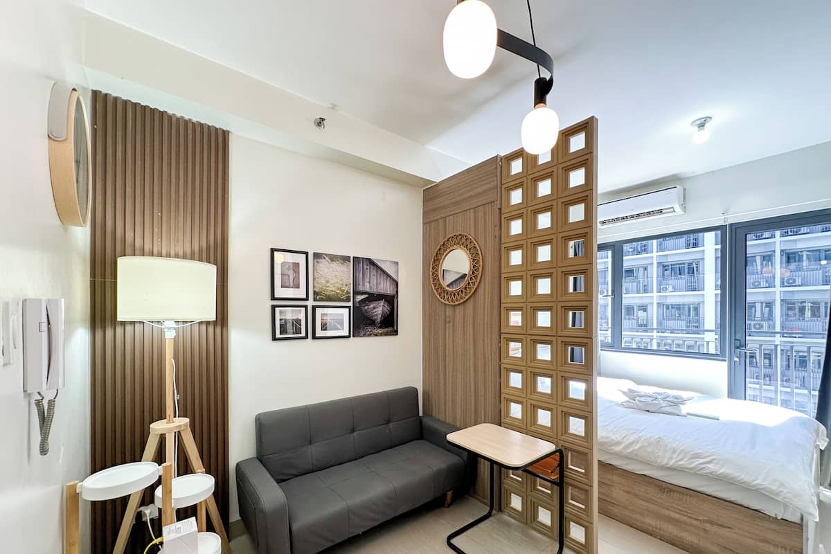 Un hotel moderno con un sofá gris, una pequeña mesa de madera, un espejo y una cama con vistas a la ciudad.