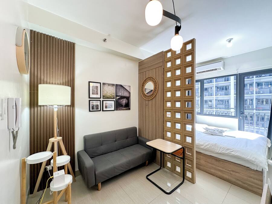 Ein modernes Hotelzimmer mit grauem Sofa, einem kleinen Holztisch, einem Spiegel und einem Bett mit Blick auf die Stadt.