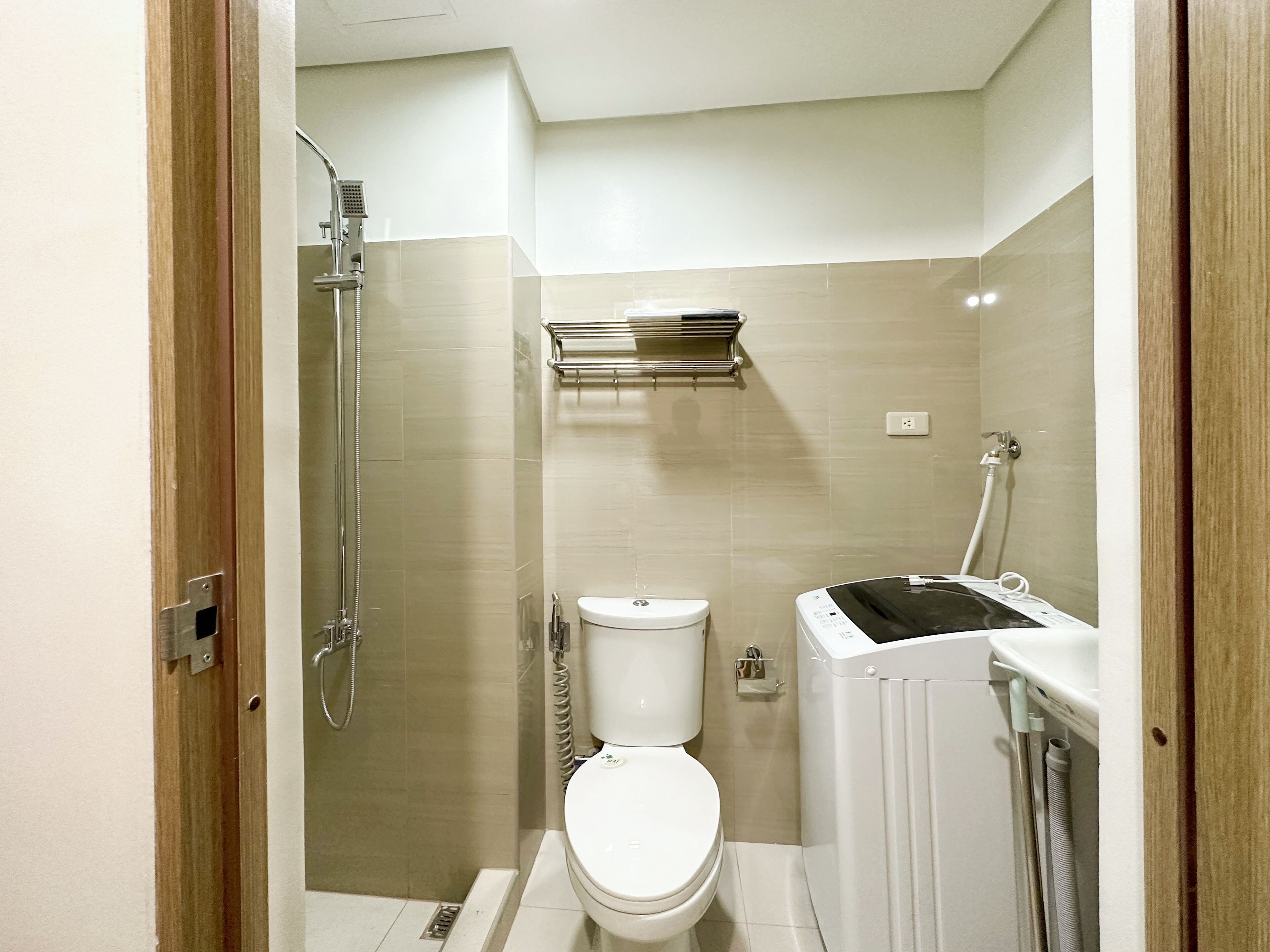 A compact bathroom with a toilet, a shower, and a built-in washing machine.