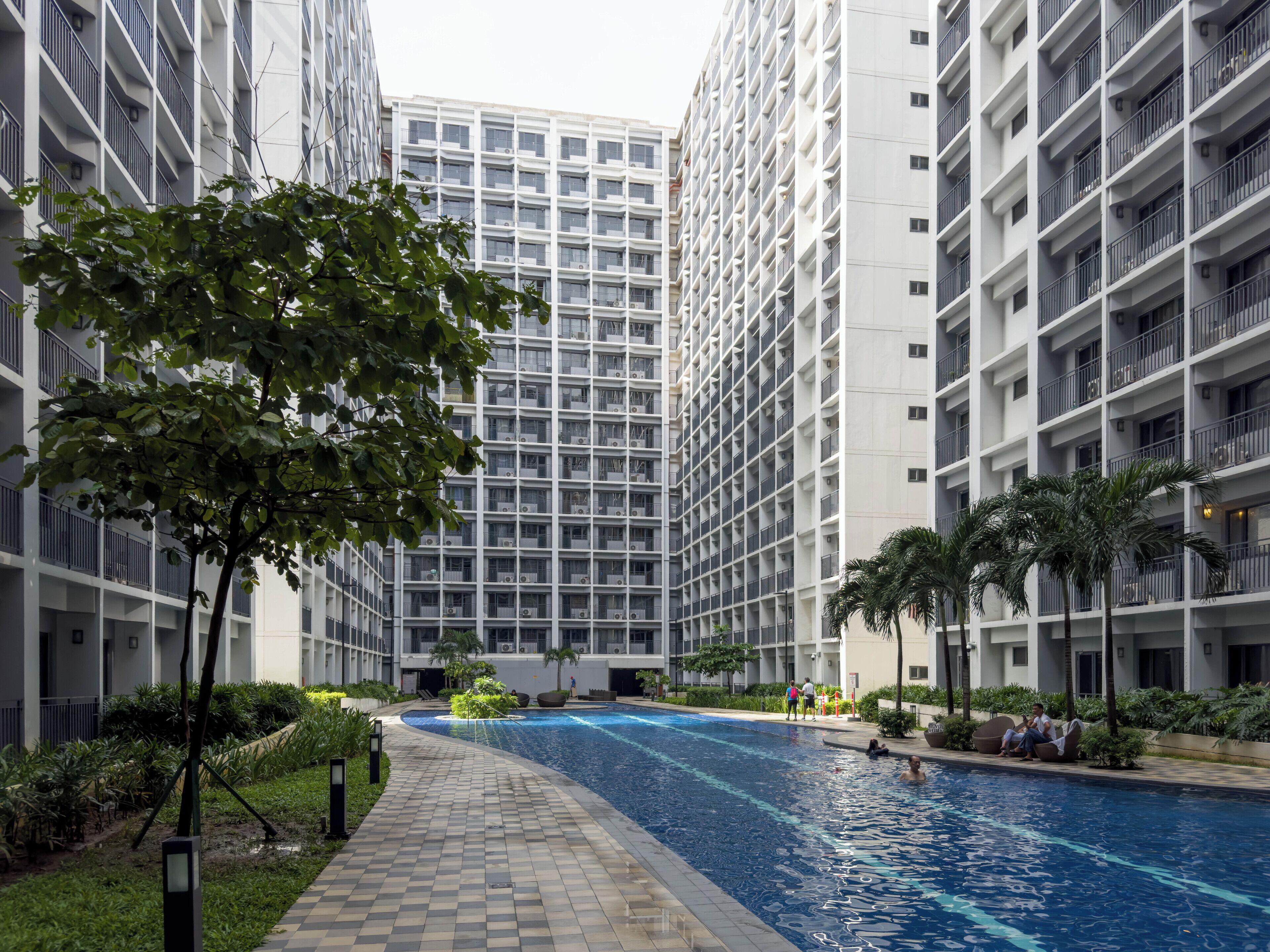 Un moderno edificio residencial con piscina central rodeada de abundante vegetación y palmeras.
