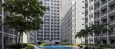 Un moderno edificio residencial con piscina central rodeada de abundante vegetación y palmeras.