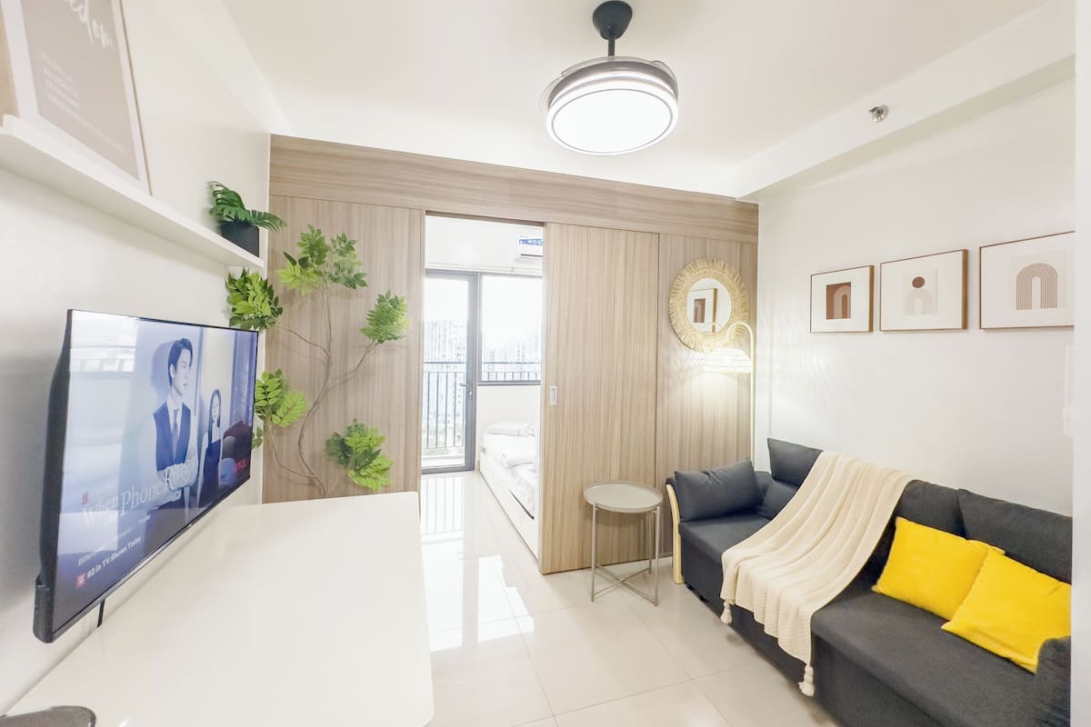 Una sala de estar moderna con un televisor de pantalla plana, un sofá, una mesita redonda y una lámpara de techo.