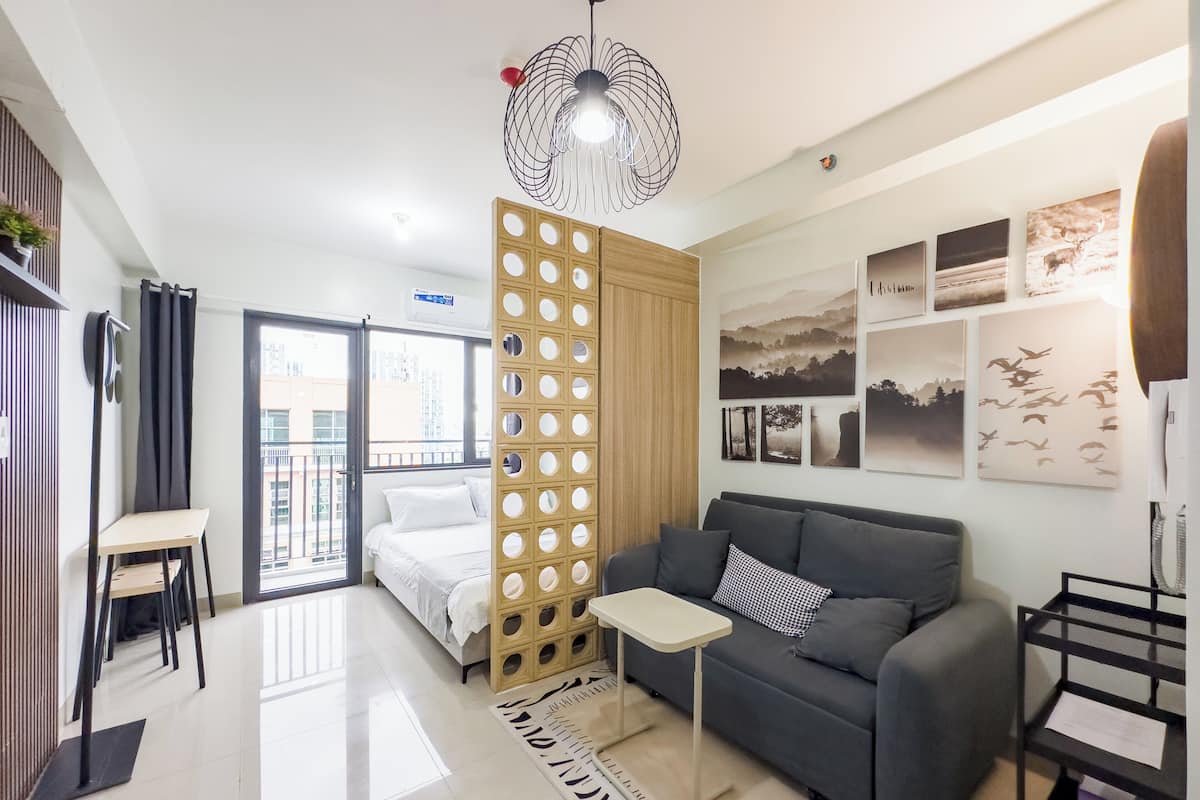 Una sala de estar moderna con un sofá gris, una mesita blanca pequeña y un separador de madera decorativo con círculos.