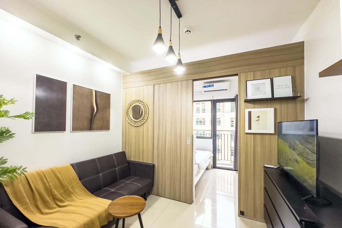 Una sala de estar moderna con un sofá, una mesita redonda, un televisor y un balcón con vistas a edificios.
