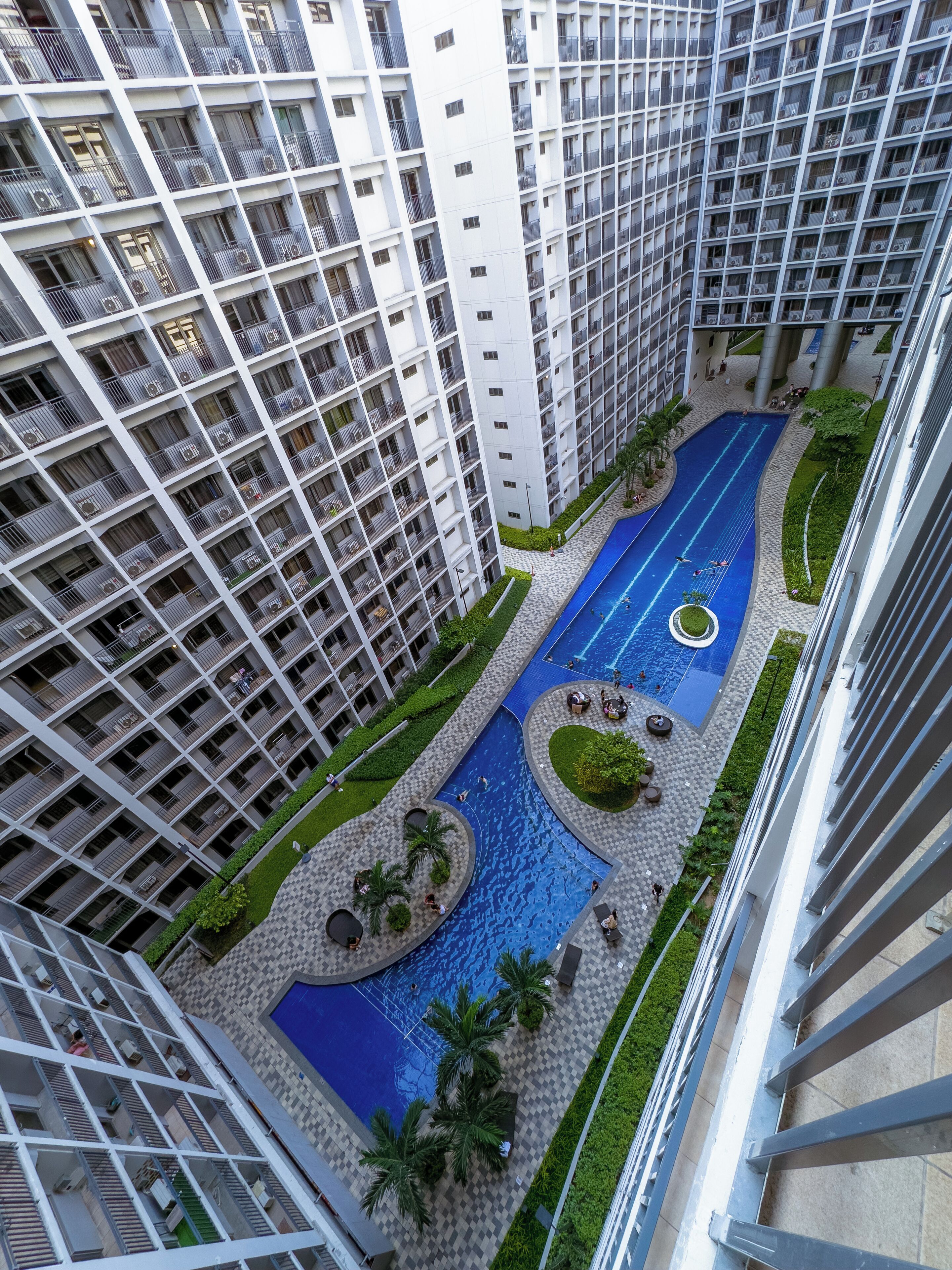 A high-rise building with multiple balconies, a central swimming pool, and surrounding greenery.