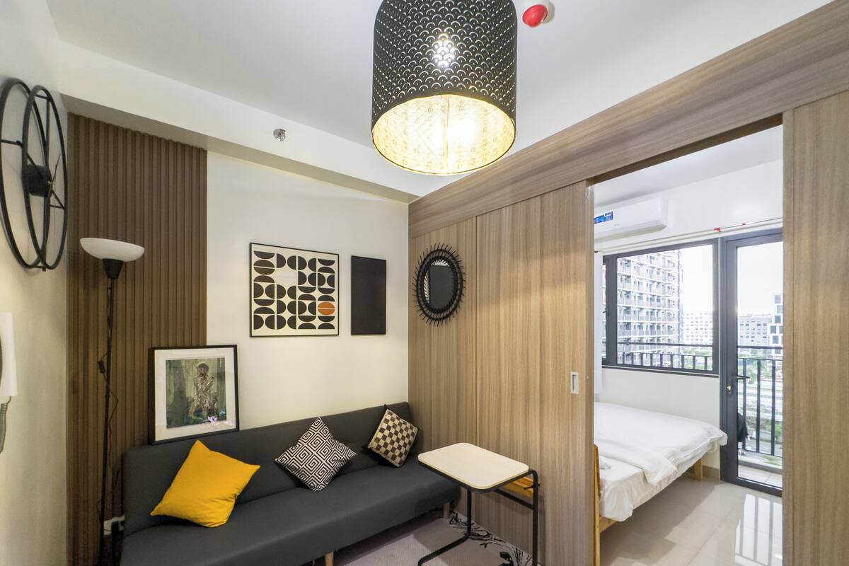 Una sala de estar moderna con un sofá, una mesita y una cama. Hay obras de arte en la pared y vistas al exterior desde un balcón.