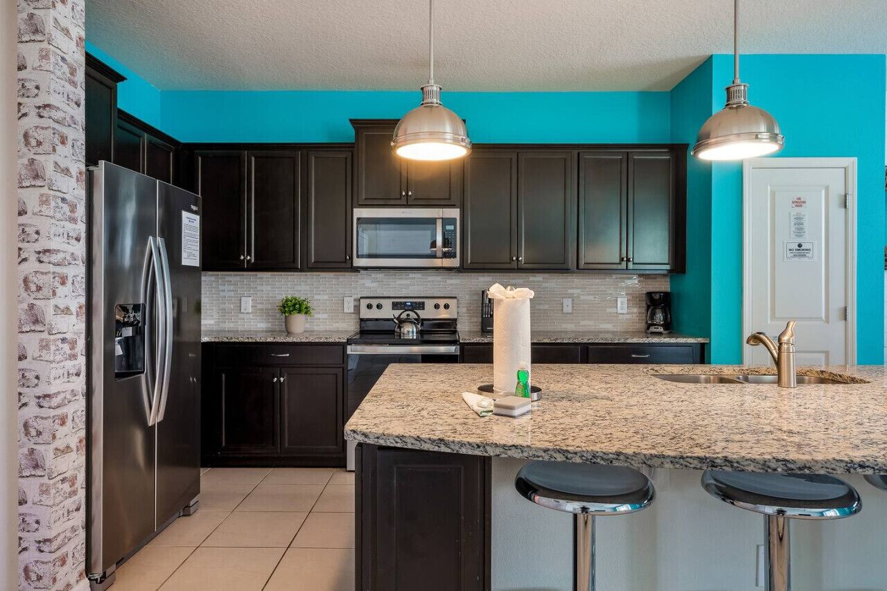 A modern kitchen with dark cabinets, a stainless steel refrigerator, a microwave, and a granite countertop.