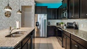 A modern kitchen with dark cabinets, a stainless steel refrigerator, a sink, and a clock on the wall. - Magic Beyond The Reef -5BR- Windsor Island- Disney (Davenport)
