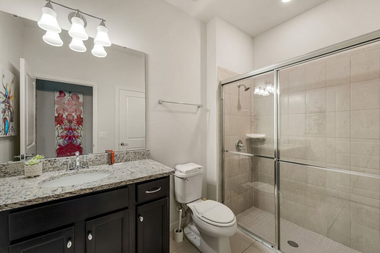 Un baño moderno con cabina de ducha de vidrio, inodoro blanco y encimera de granito con lavabo.