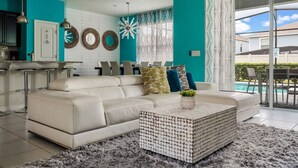 A modern living room with a white sofa, a coffee table, and a view of a swimming pool. - Magic Beyond The Reef -5BR- Windsor Island- Disney (Davenport)