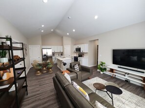 A modern living room with a sofa, TV, and a dining area with a table and chairs. - Cozy 3-Bedroom Duplex (Wichita)