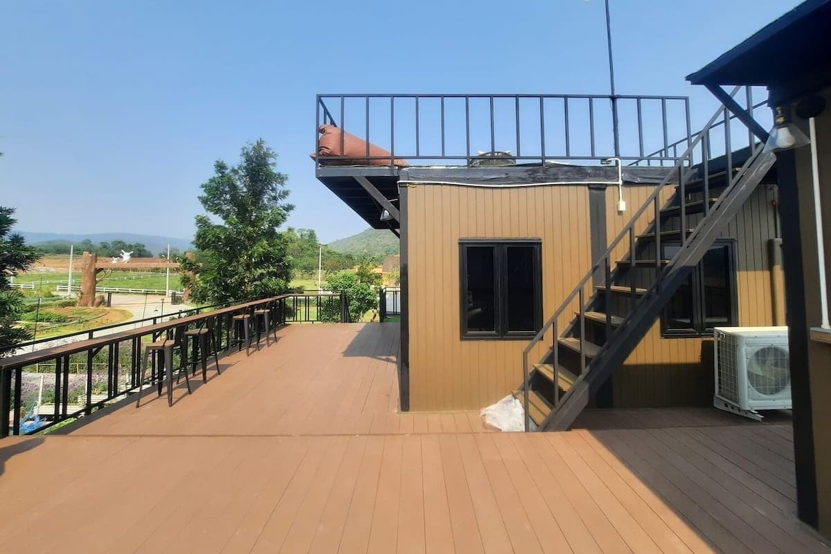 A wooden deck with a metal railing, a staircase, and a small building with a window.