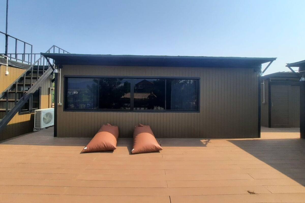 A modern building with a large window and a small porch area with two cushions.