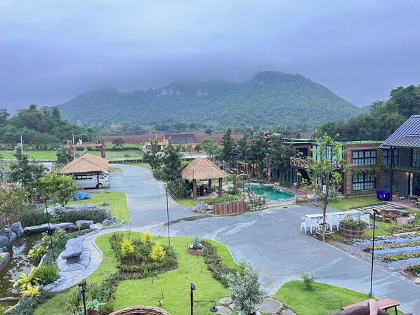 A resort with a swimming pool, thatched-roof structures, and a view of a mountain.