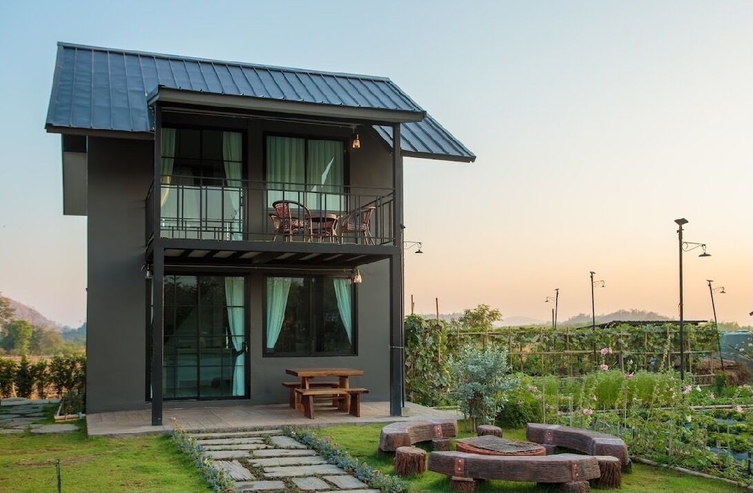 A two-story modern house with a balcony, a wooden bench, and a garden with plants and a stone pathway.