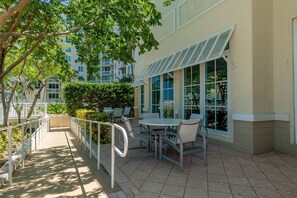 Un espace patio extérieur avec une table et des chaises, entouré d’une balustrade blanche et de verdure.