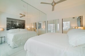 Une chambre d’hôtel moderne avec un grand lit, un ventilateur de plafond et un tableau représentant un paysage urbain accroché au mur.
