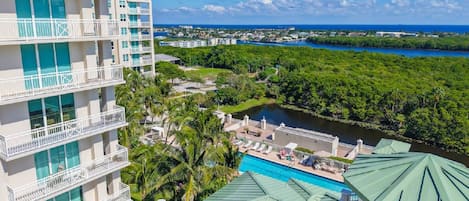 A multi-story hotel with balconies, a swimming pool, and a view of a river and greenery.