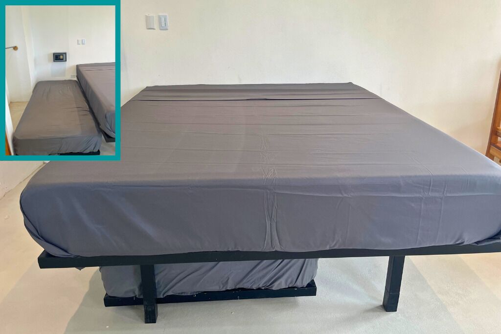 Una cama individual con colchón gris y estructura negra en una habitación con paredes blancas y suelo de tonos claros.