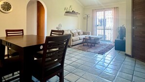 A dining area with a table and chairs, a ceiling fan, a clock, and a living room with a sofa and a coffee table. - Cozy Apartment Near the Beach (Mazatlán)