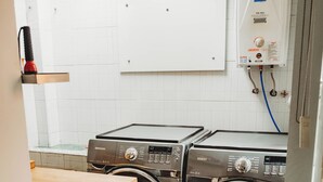 Une buanderie équipée de deux machines à laver Samsung, d’un chauffe-eau et d’une étagère en bois.