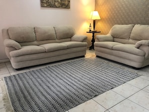 A living room with two beige sofas, a patterned rug, a small side table with a lamp, and a wall with a geometric pattern.