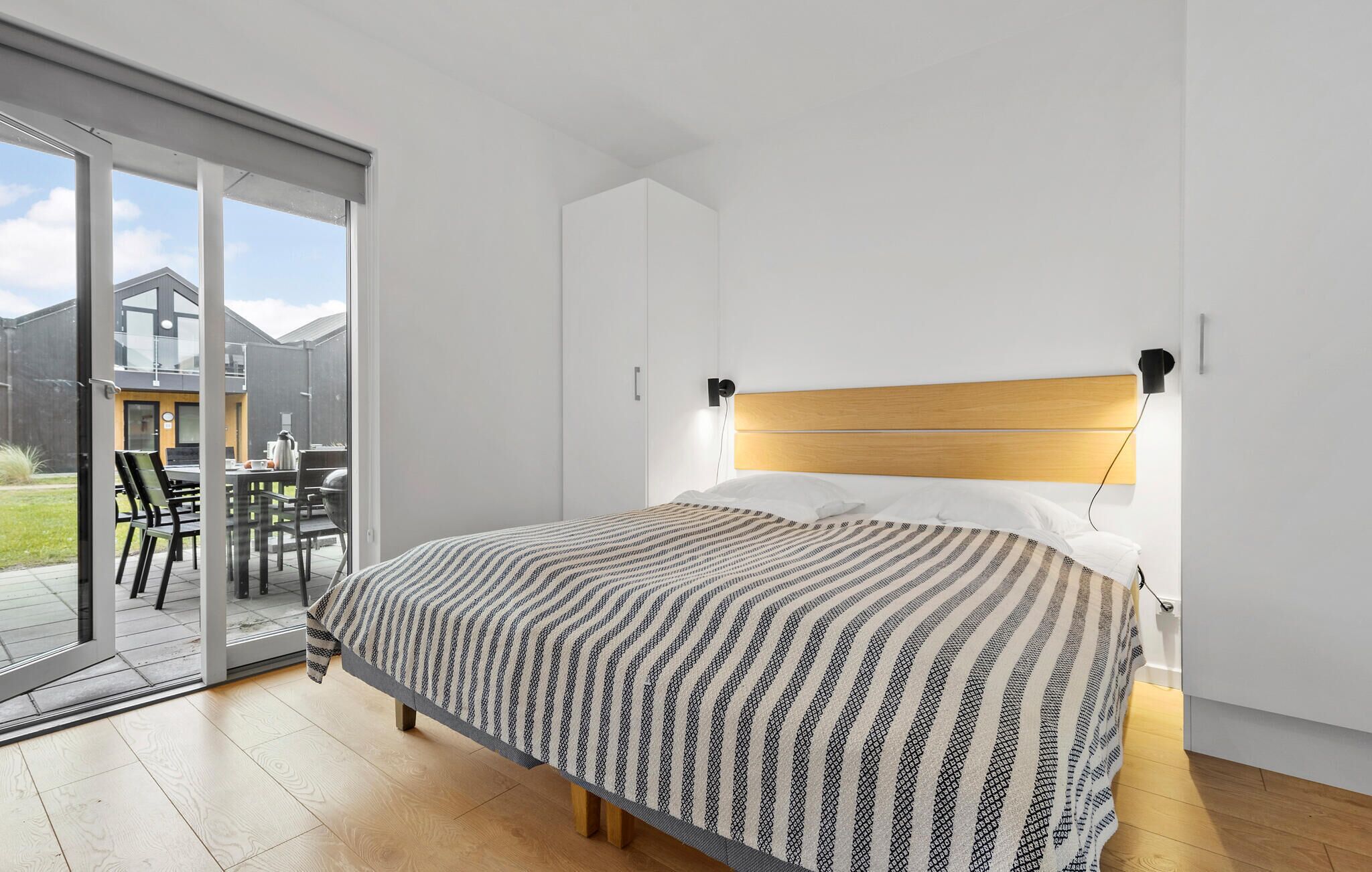 A modern bedroom with a large bed, a wooden headboard, and a sliding glass door leading to an outdoor area with a table and chairs.
