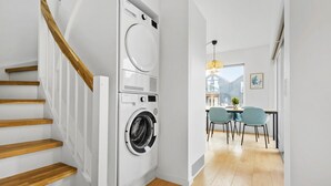 A modern kitchen with a built-in washing machine, wooden staircase, and a dining area with chairs and a table. - Lovely apartment in Slagelse (Slagelse)