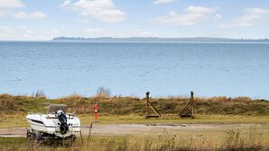 A boat on a trailer near a body of water with a grassy area and a red and white pole in the foreground. - Lovely apartment in Slagelse (Slagelse)