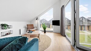 A modern living room with a sofa, a round table, and a TV. There are large windows and a view of a residential area. - Lovely apartment in Slagelse (Slagelse)