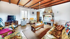A cozy living room with a stone fireplace, wooden ceiling beams, a television, and comfortable seating.