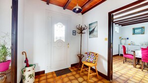 A room with a wooden ceiling, a white door, a coat rack, a chair with a colorful cushion, and a tiled floor.