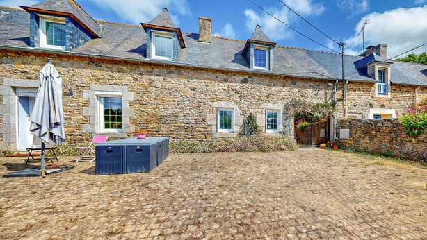 A stone building with multiple windows, a covered patio area, and a cobblestone courtyard.