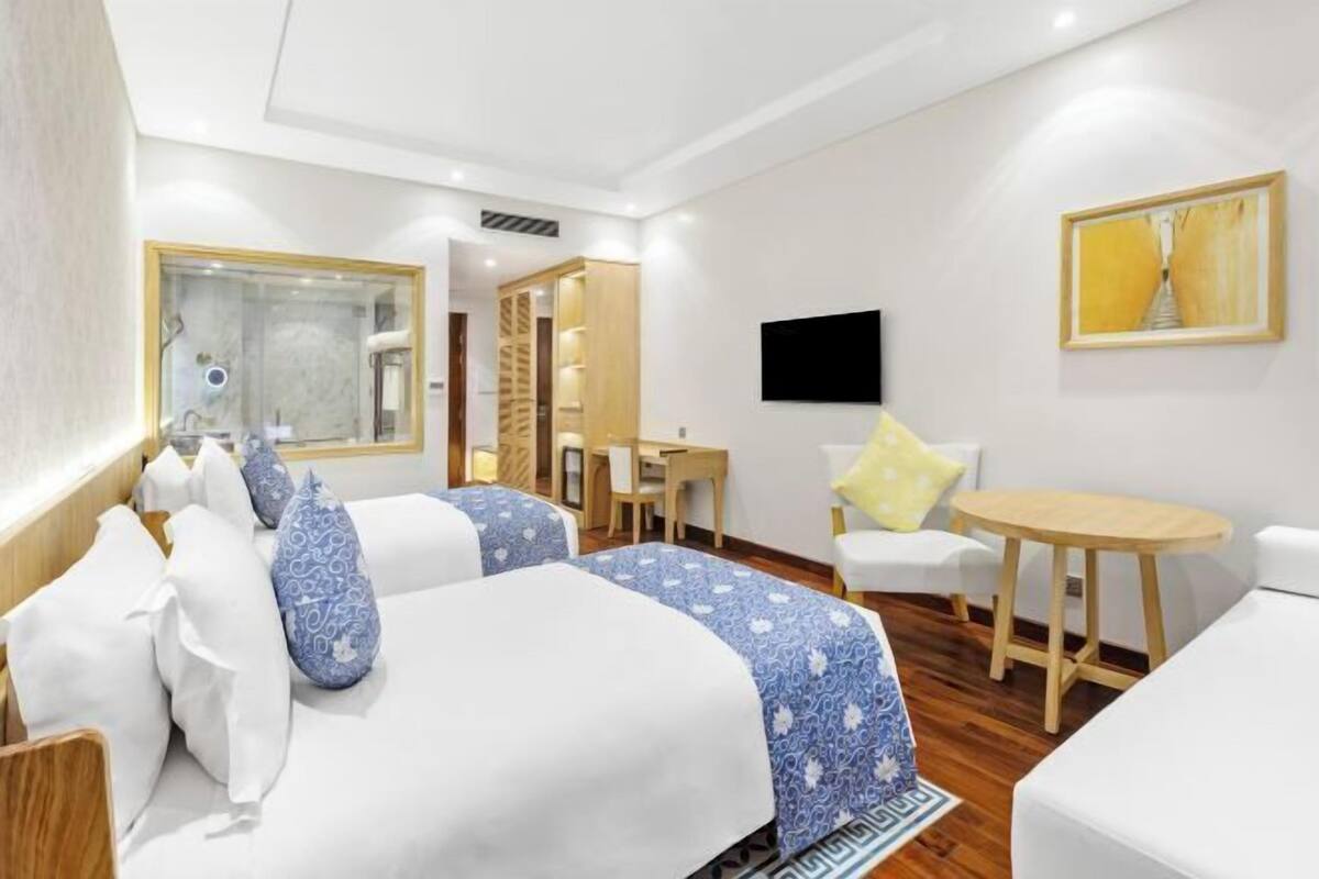 A hotel room with two beds, a desk, a chair, a TV, and a painting on the wall.