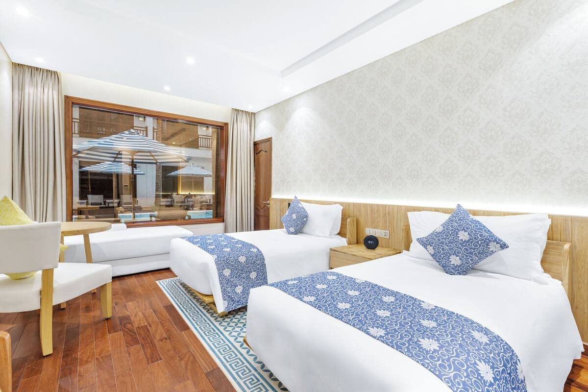A hotel room with two beds, a sofa, a small table, and a large window with curtains.