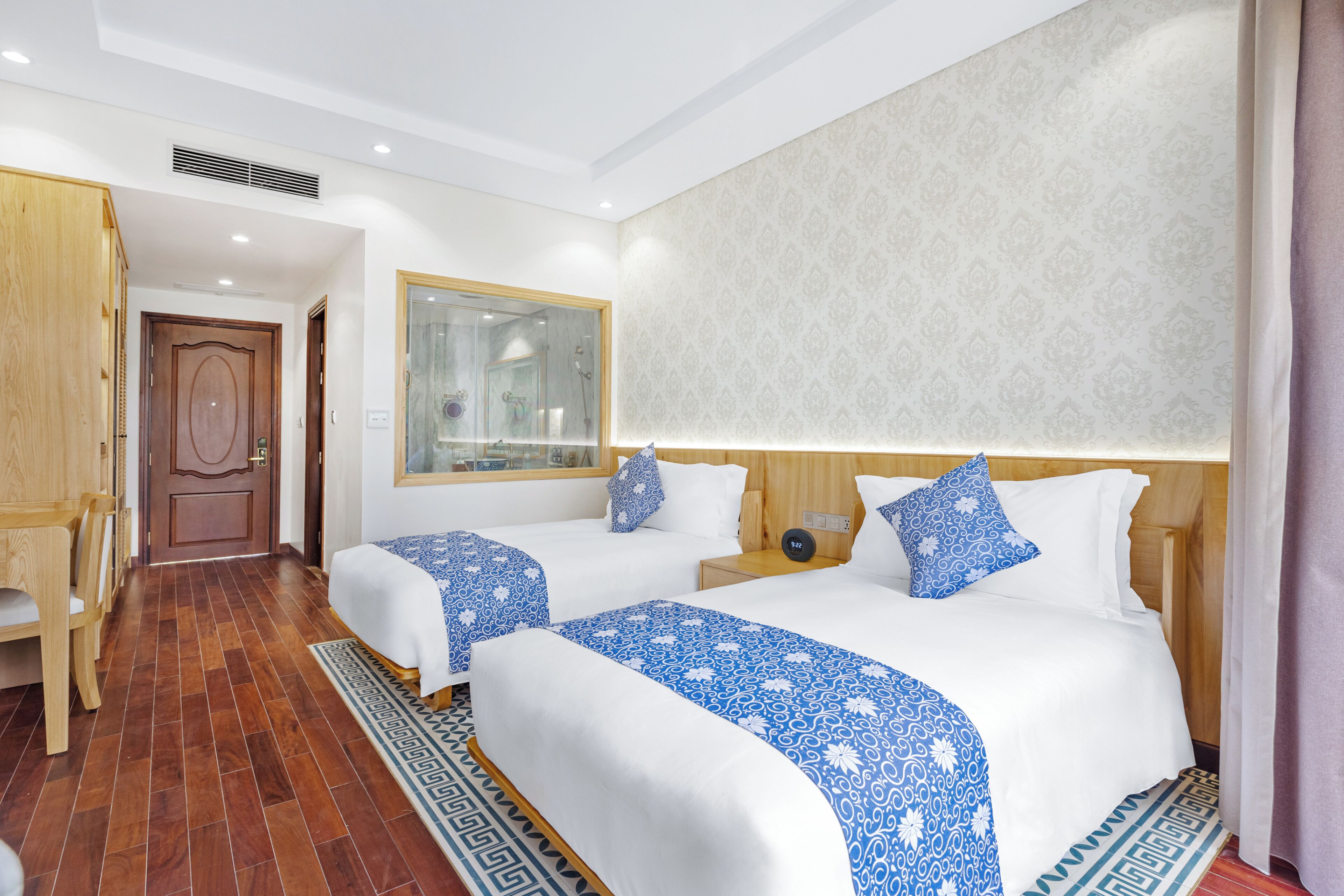 A hotel room with two beds, a wooden wardrobe, a mirror, and a patterned wall.