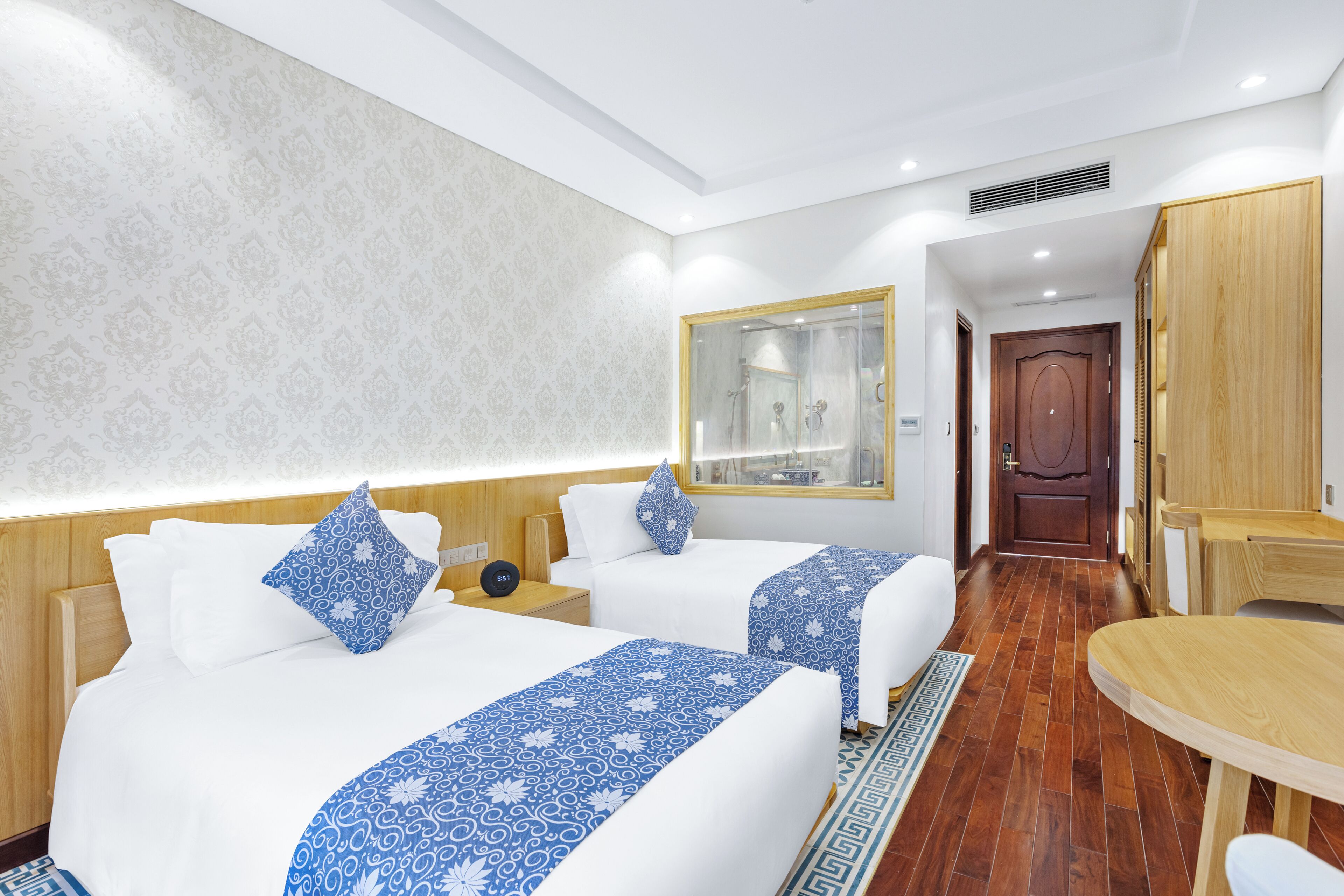 Ein Hotelzimmer mit zwei Betten, einem Holzkopfteil, einem Spiegel, einem Holztisch und einem gemusterten Teppich.