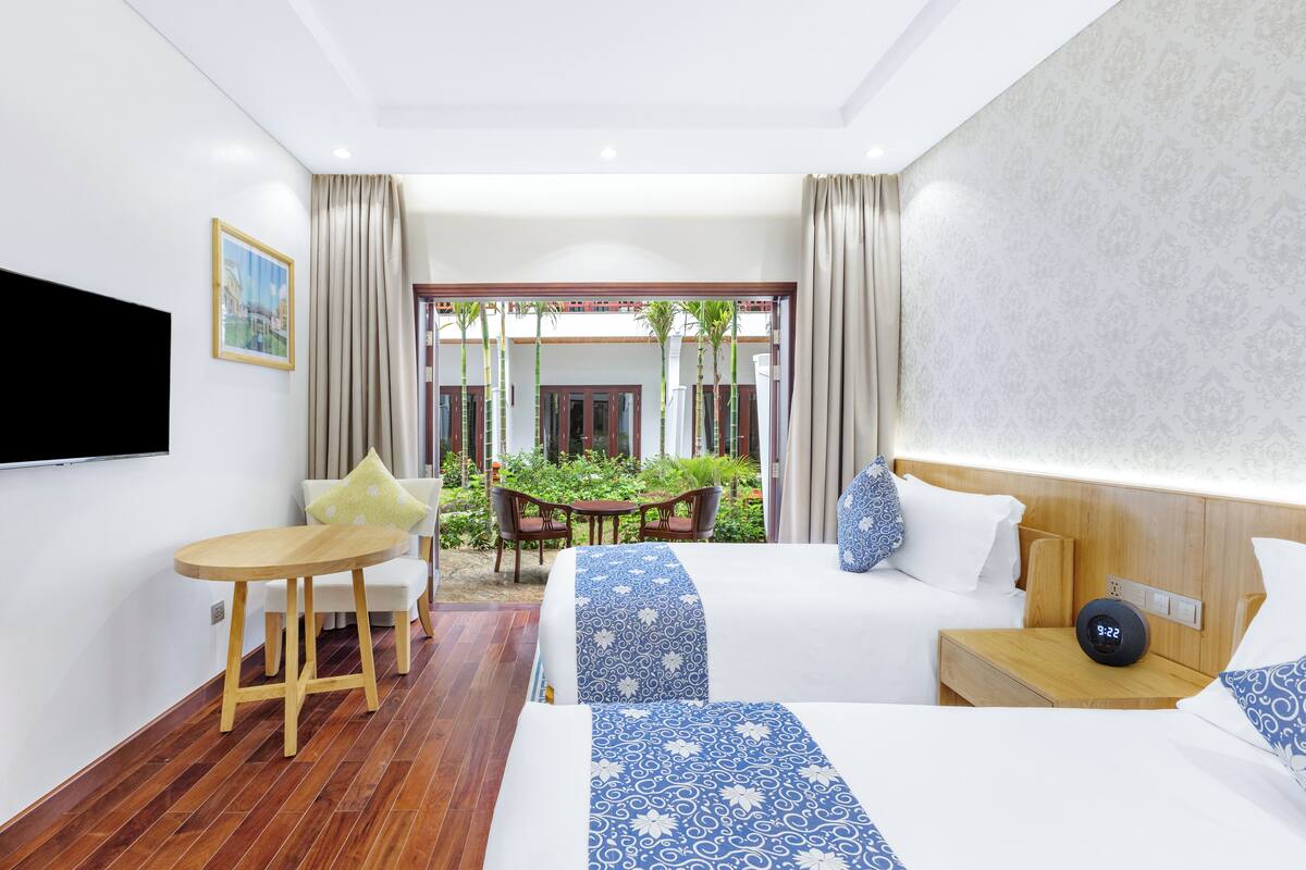 A hotel room with a bed, bedside table, TV, and a small balcony with a table and chairs.