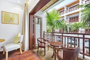 A balcony with wooden furniture, a view of a building with balconies, and a plant. - Wafaifo Resort Hoi An (Da Nang)