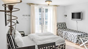 Et hotelværelse med seng, skrivebord, stol, fjernsyn og et vindue med gardiner.
