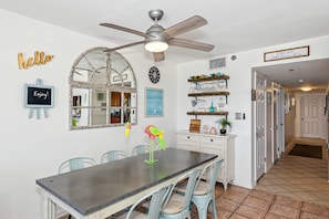A kitchen with a dining table, chairs, a ceiling fan, decorative mirrors, and a wall with motivational signs.