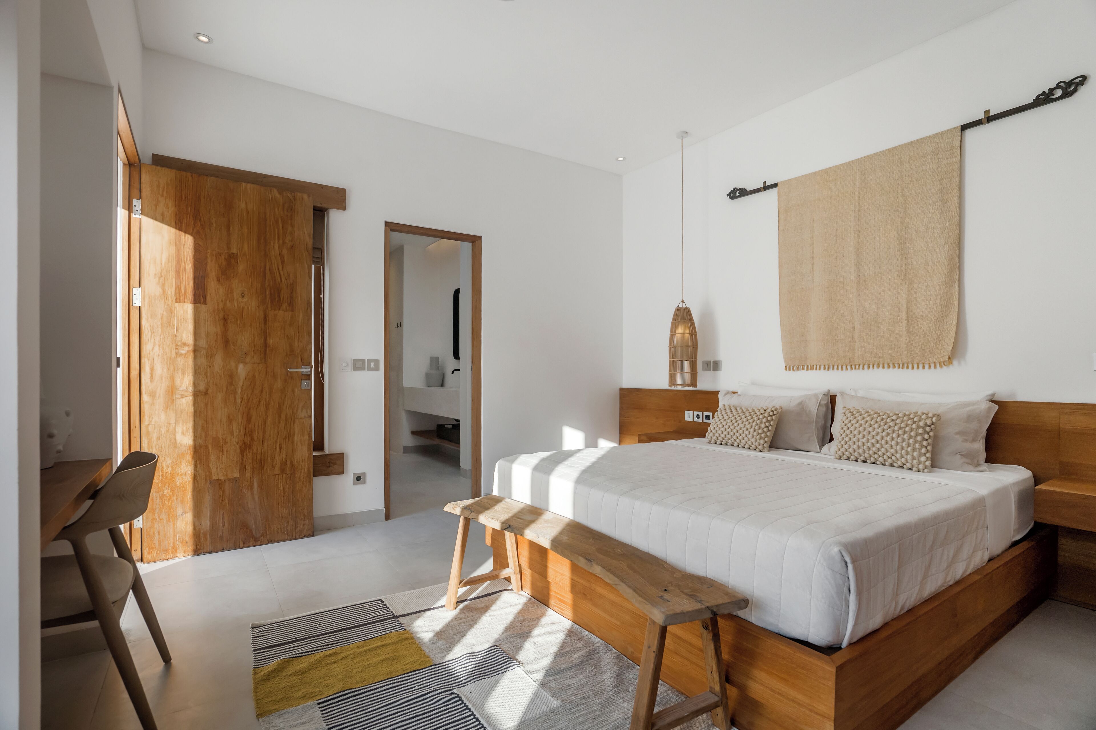 Ein modernes Schlafzimmer mit einem Holzbettgestell, einer Bank, einem großen Fenster und Blick auf den Flur.