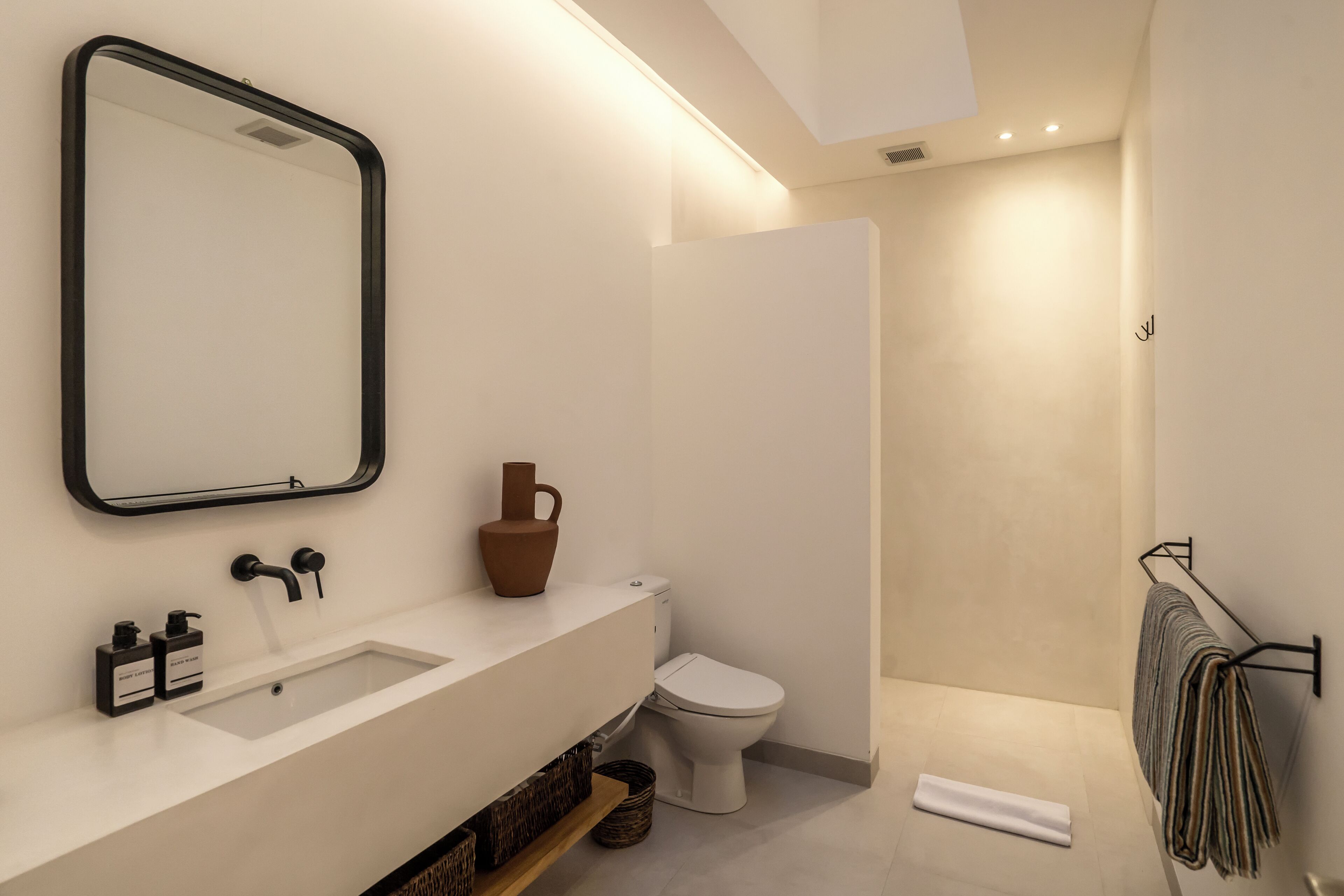 Un baño moderno con lavamanos blanco, grifo negro y un espejo grande.