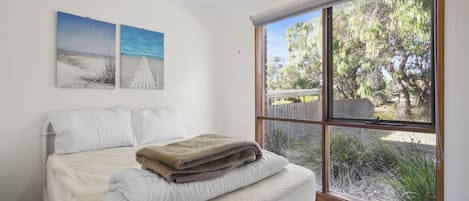 Une chambre à coucher avec un lit, une fenêtre donnant sur des arbres et une clôture, et deux tableaux accrochés au mur.
