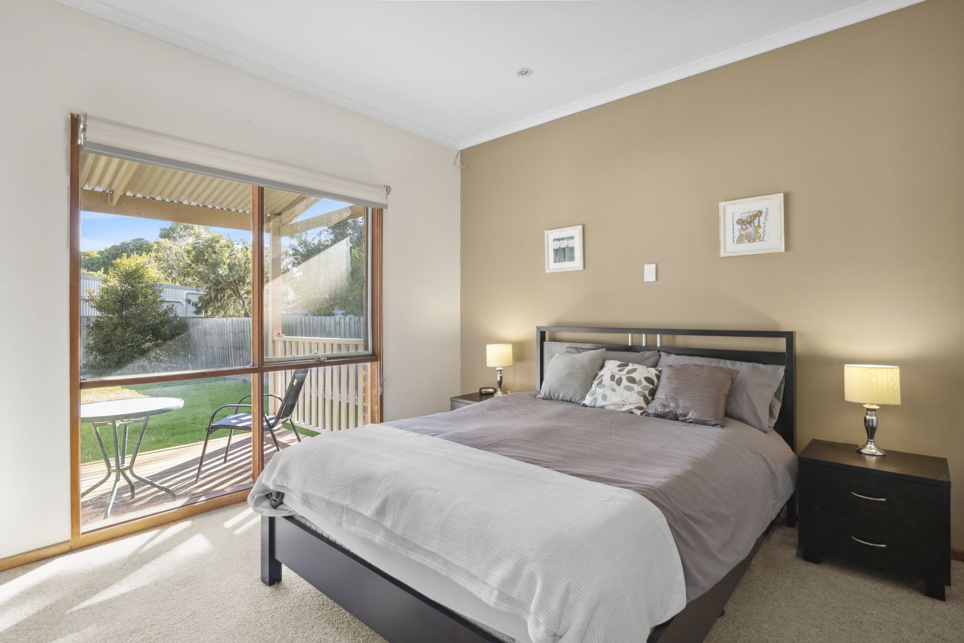 A bedroom with a bed, two bedside tables, a window, and a view of the outdoors.