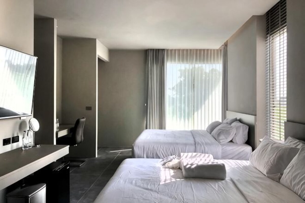 Een hotelkamer met twee bedden, een bureau met stoel, een televisie en een raam met jaloezieën.